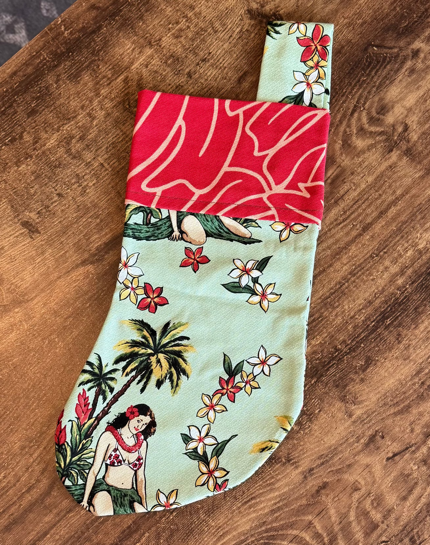 Christmas stocking made from Hawaiian-themed fabric on a wooden surface